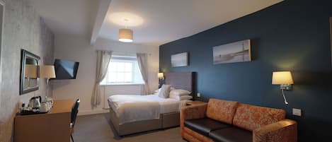 Una habitación de hotel con cama, escritorio, sillón, sofá y televisor fijado a la pared.