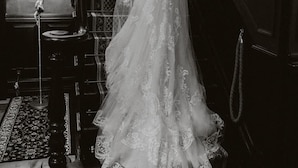 Uma noiva num vestido branco desce uma escadaria imponente, com um candeeiro e quadros nas paredes.