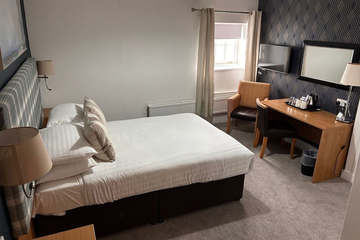 Una habitación de hotel con cama, escritorio, silla, lámpara y un espejo grande.