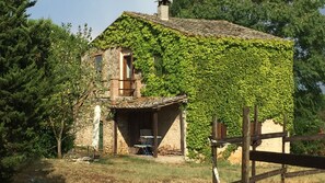 A rustic stone house with ivy covering the exterior walls, a small porch with a table and chairs, and a wooden fence in the foreground. - Agriturismo Podere Conte Ràcani - Appartment IL GRANAIO (Amelia)