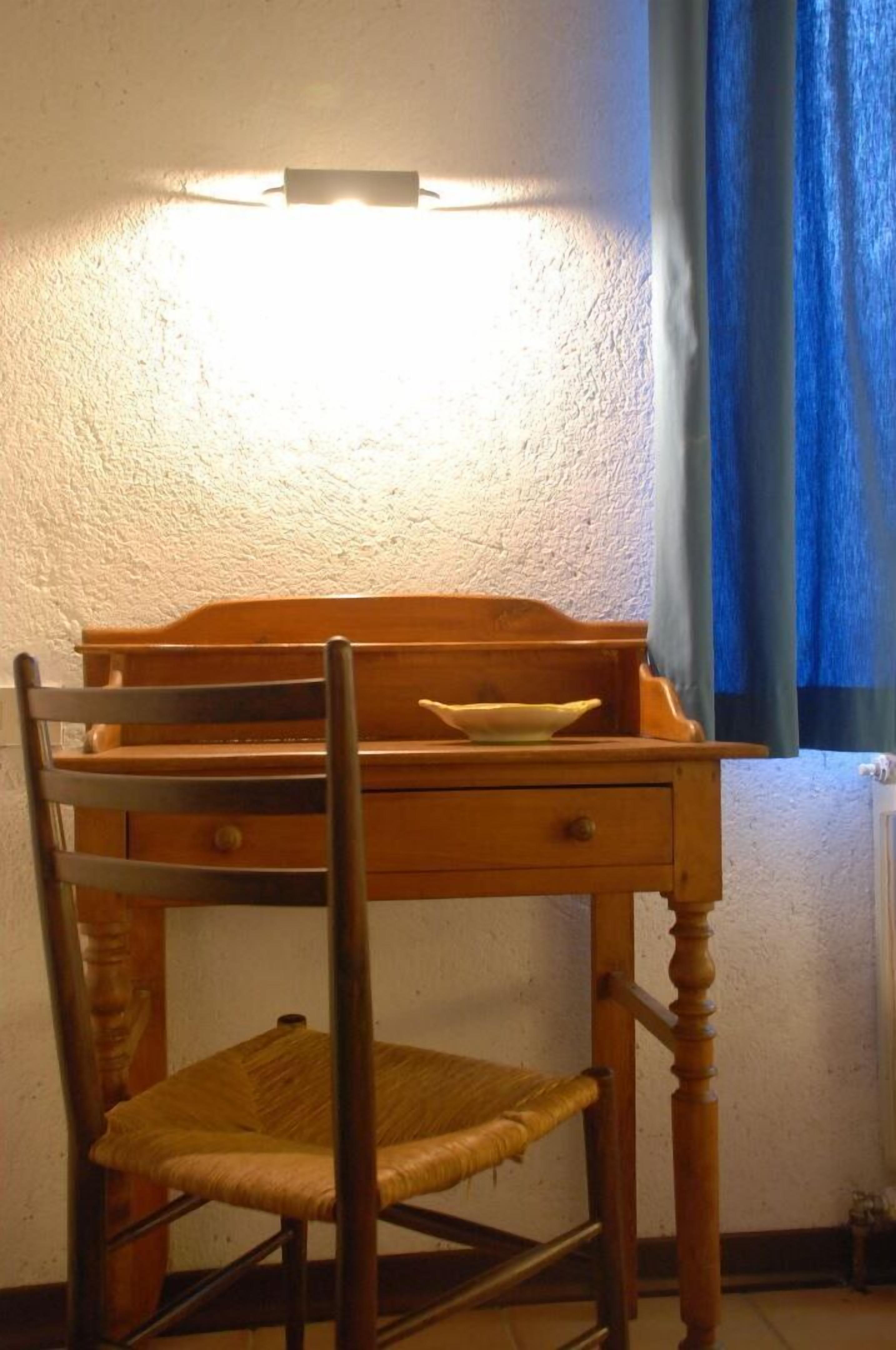 Puisesta pöydästä, tuolista, pienestä kulhosta ja seinään kiinnitetystä valaisimesta koostuva kokonaisuus.