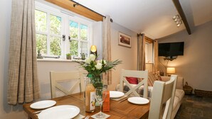 A dining area with a wooden table set for two, a vase with flowers, and a television mounted on the wall. - The Old Bakehouse (Leominster)
