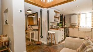 A spacious living area with a high ceiling, a kitchen with white cabinets, and a dining area with a wooden table and chairs. - The Old Bakehouse (Leominster)