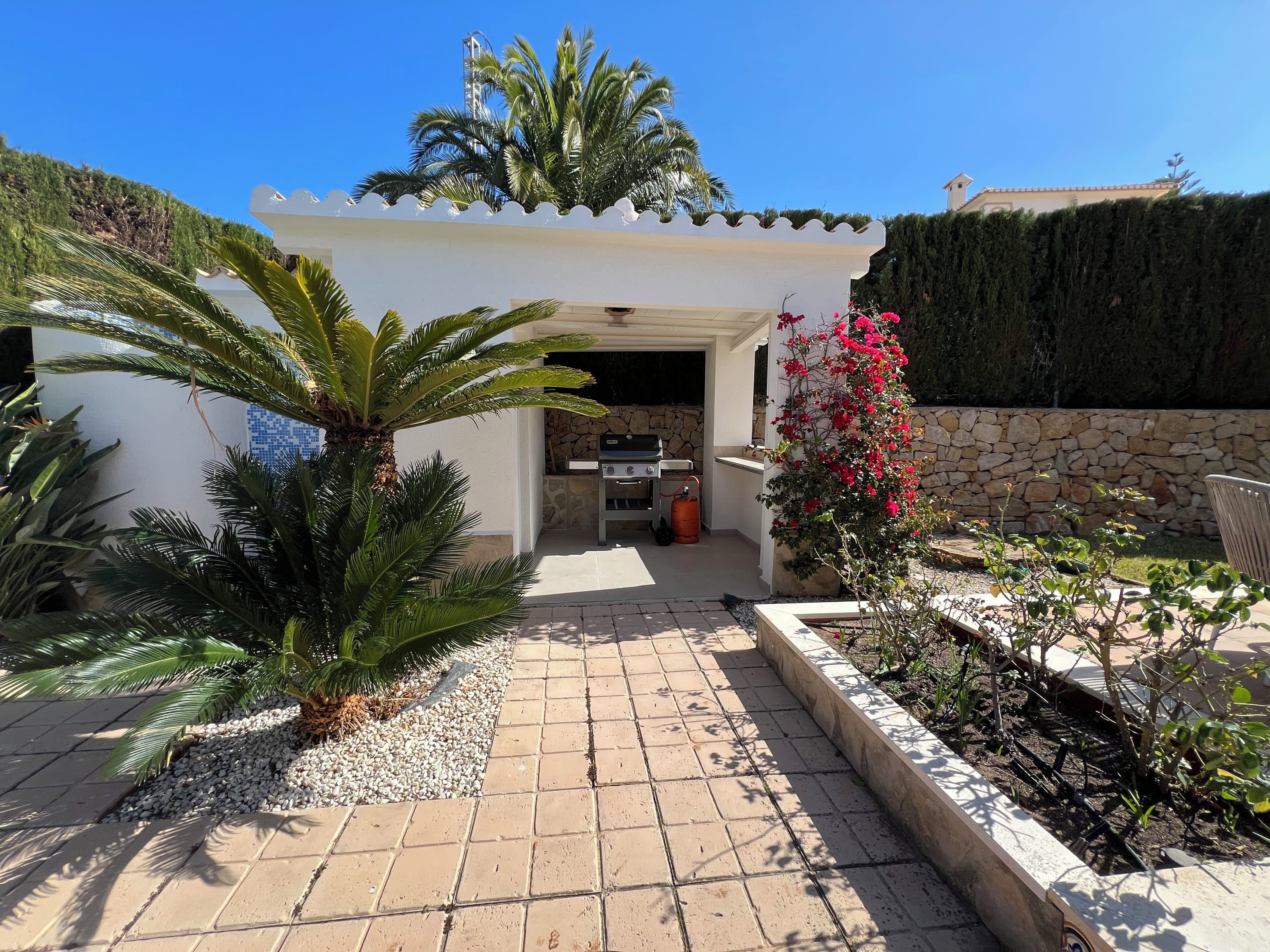 A patio area with a grill, potted plants, and a stone wall.