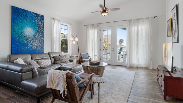 A modern living room with a leather sofa, a round coffee table, and a ceiling fan. - Tranquil Tides, an exquisite beach home on Hill St with beach access directly across street! (New Smyrna Beach)