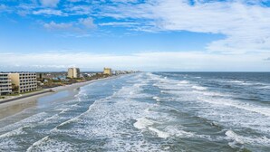 A coastal hotel with multiple buildings along the beachfront, featuring a sandy beach and ocean view. - Tranquil Tides, an exquisite beach home on Hill St with beach access directly across street! (New Smyrna Beach)