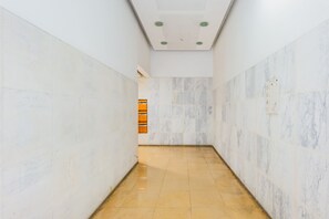 A corridor with marble walls and a tiled floor, leading to a room with a door and a window. - Hang your Hat (Lisbon)