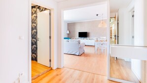 Un appartement moderne avec un plancher en bois, un espace de vie comprenant un canapé et un téléviseur, et une cuisine à l’arrière-plan.