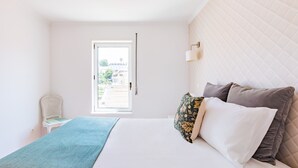 Une chambre à coucher avec un lit, une fenêtre, une chaise et un luminaire fixé au mur.