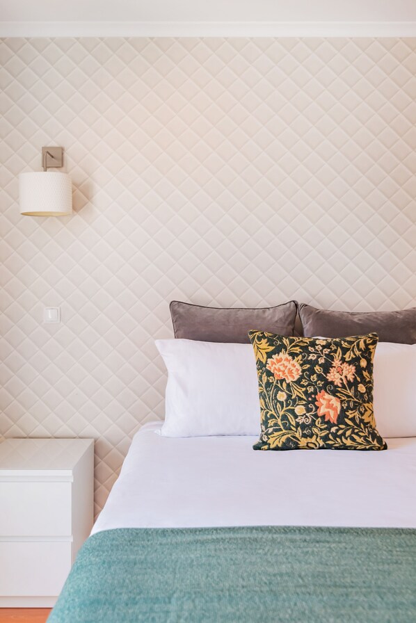 Un lit bien fait, avec des oreillers blancs et bruns, un plaid vert et un coussin à motifs floraux.