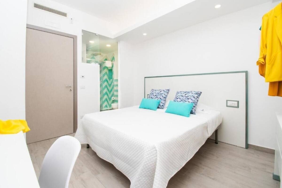Moderni hotellihuone, jossa on sänky, tuoli ja vaatekaappi.