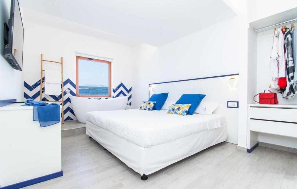 Ein Schlafzimmer mit einem Bett, einem Schreibtisch, einem Fernseher, einem Fenster mit Aussicht und einem Kleiderständer.