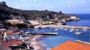 Un pueblo costero con un puerto deportivo, acantilados rocosos y un edificio histórico en una colina.