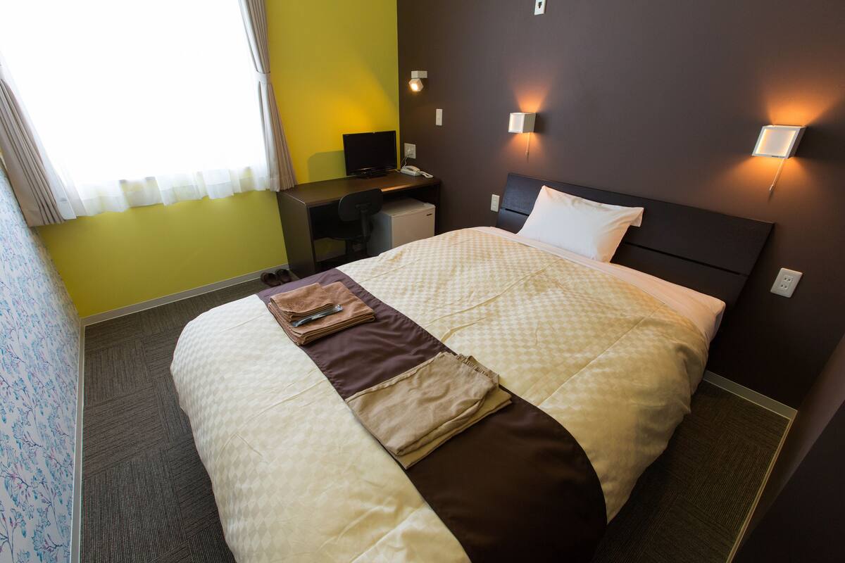 A hotel room with a bed, a desk, a chair, and a small refrigerator.