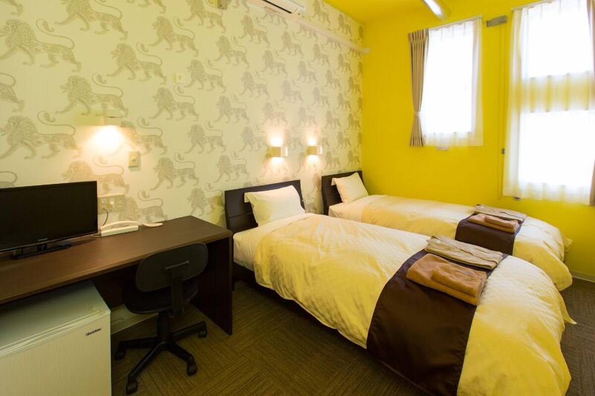 A hotel room with two beds, a desk, a chair, and a television.