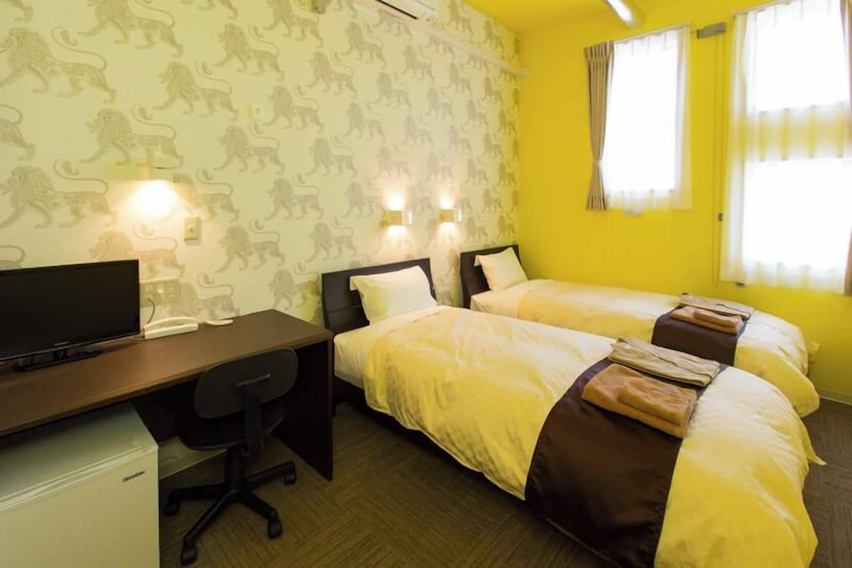 A hotel room with two beds, a desk, a chair, and a television.