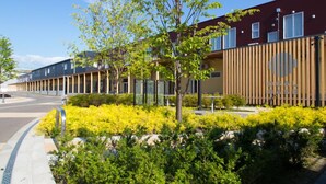 A modern building with a mix of wooden and glass facades, a landscaped garden with yellow shrubs, and a clear sky. - OGAL INN (Shiwa)