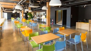 A modern cafeteria with multiple tables and chairs, a large plant, and a counter area. - OGAL INN (Shiwa)
