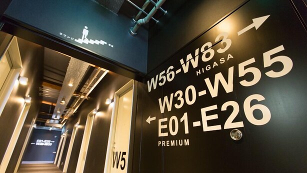 A hotel corridor with directional signs for rooms W56-W83, W30-W55, and E01-E26, labeled as premium. - OGAL INN (Shiwa)