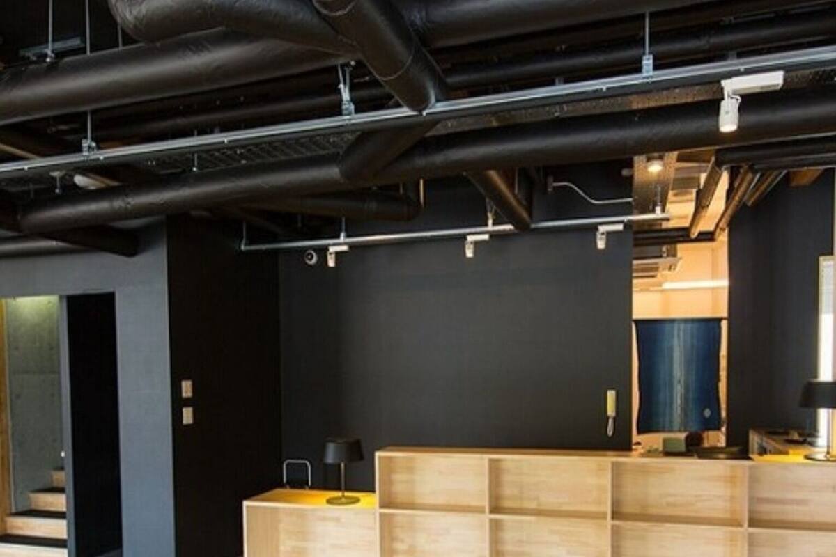 Un intérieur moderne avec des conduits apparents, un comptoir d’accueil et un escalier menant à un niveau supérieur.