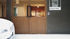 Habitación de hotel con puerta de madera, un coche blanco estacionado afuera y una pared con los números de habitación 31, 33 y 35.