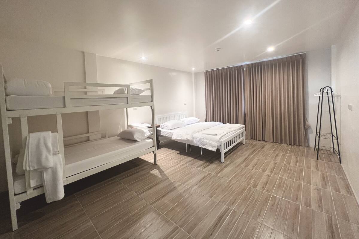 A room with bunk beds, a single bed, a curtain, and a standing lamp.