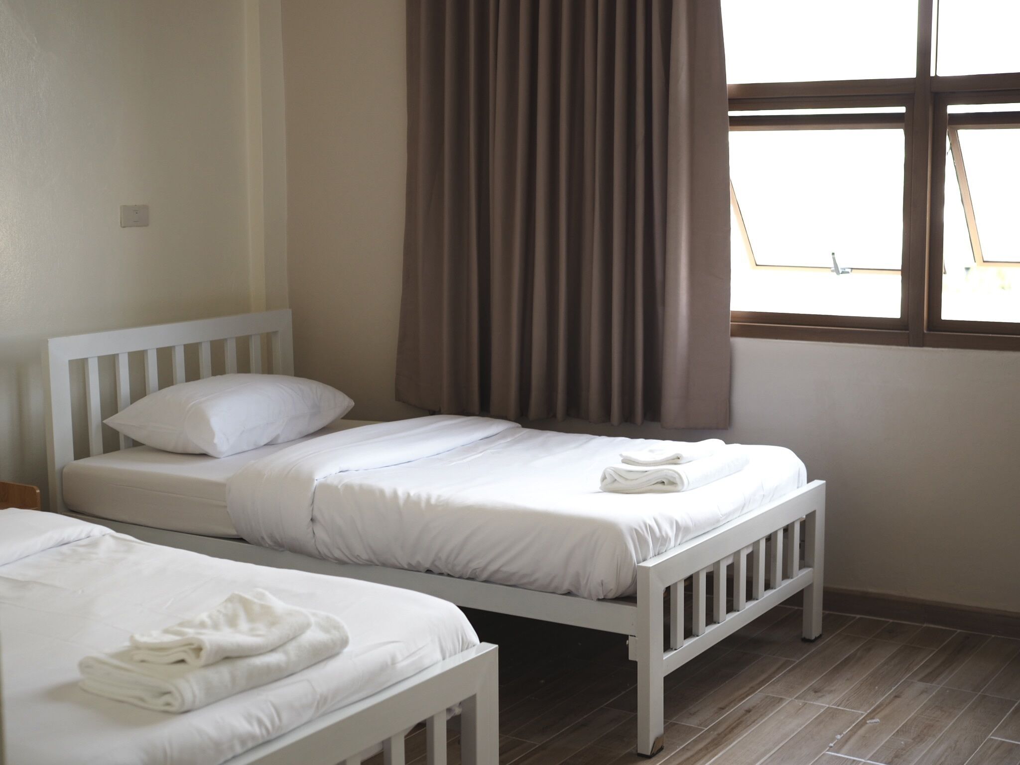 A room with two single beds, each with white bedding and pillows, and a window with curtains.