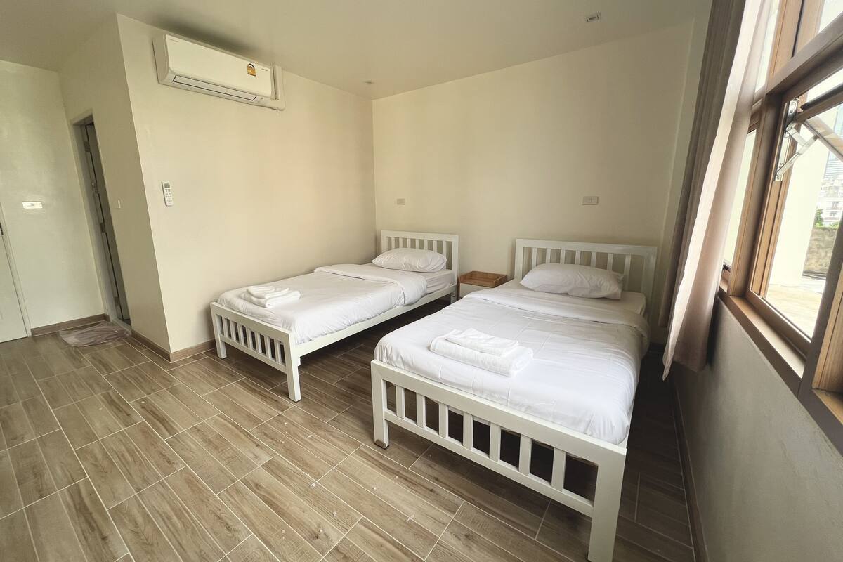 A clean, well-lit room with two single beds, a window, and a door.