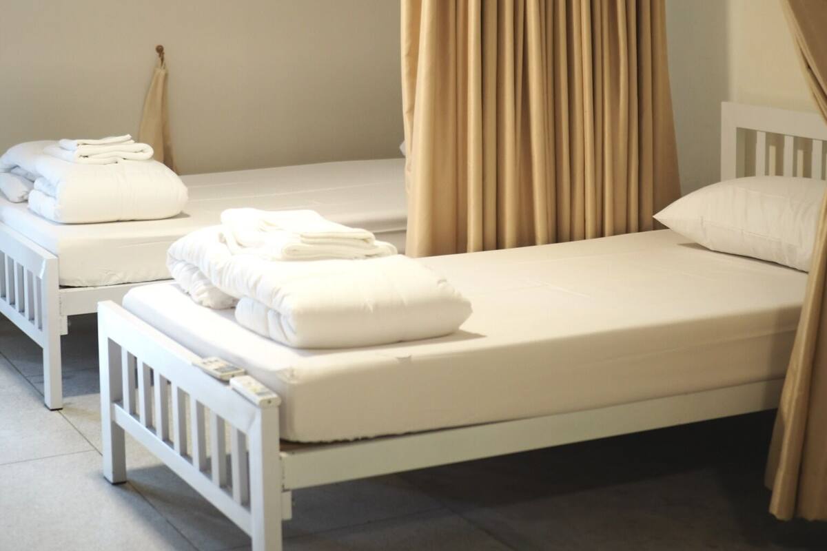 A single-bed room with a white frame, beige curtains, and neatly folded white towels on the bed.