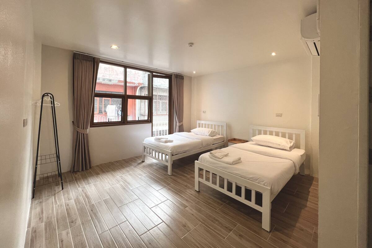 A bedroom with two single beds, a window with curtains, a radiator, and a wooden floor.