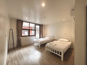 A bedroom with two single beds, a window with curtains, a radiator, and a wooden floor. - Krung Tone Hostel (Bangkok)