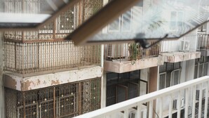 Un edificio de varios pisos con balcones, barandillas metálicas y unidades de aire acondicionado.