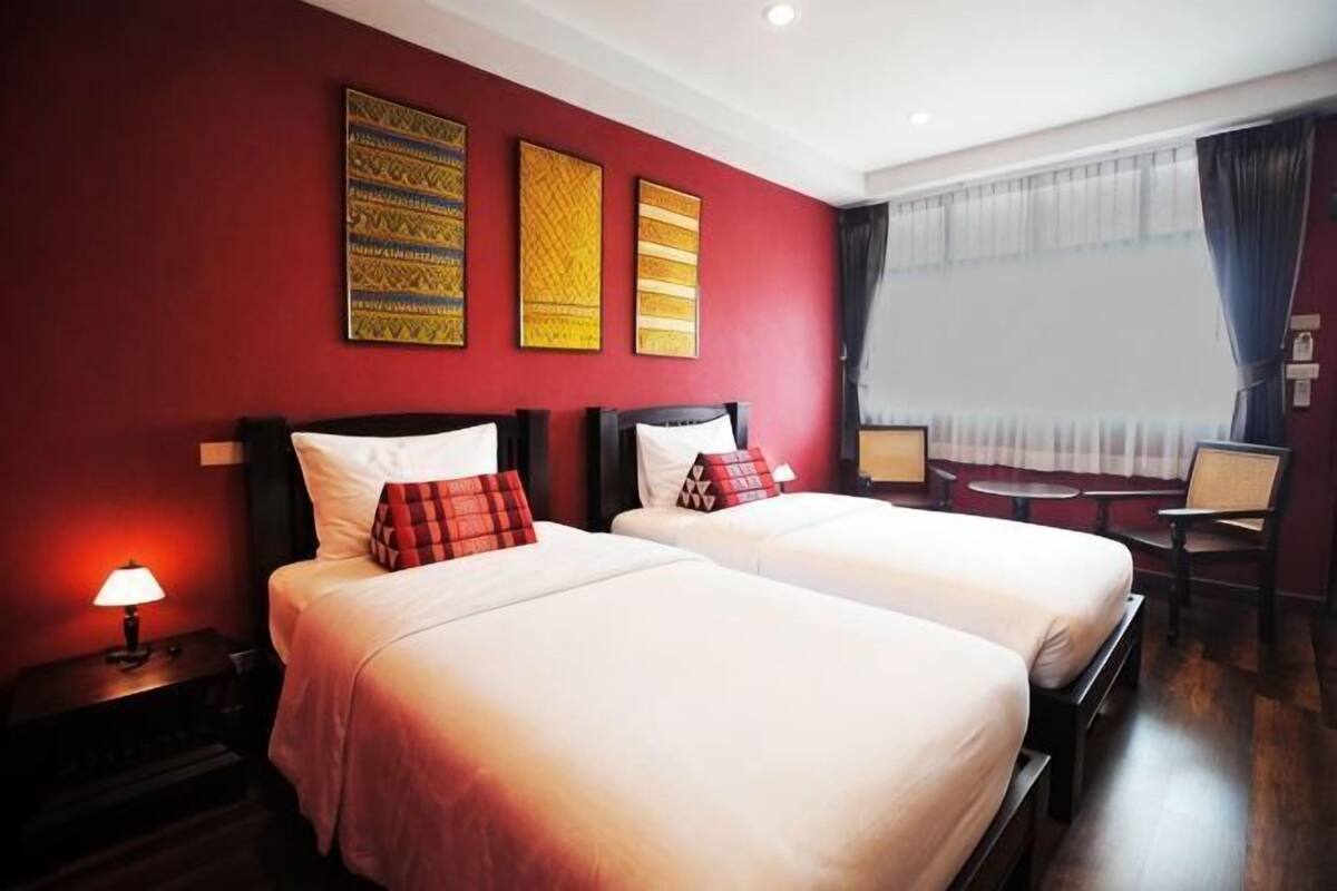 A hotel room with two beds, a desk, a chair, and a window with curtains.