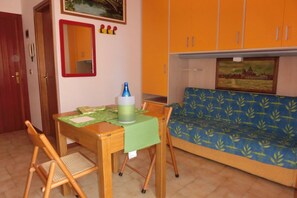 Ein kleiner Raum mit einem Bett, einem Tisch mit Stühlen, einem Spiegel und einem Bild an der Wand.