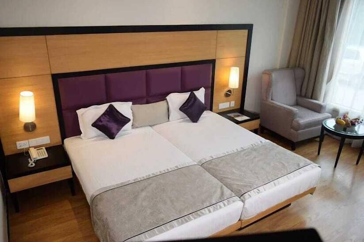 A hotel room with a large bed, two bedside tables, a chair, and a small table with a lamp.