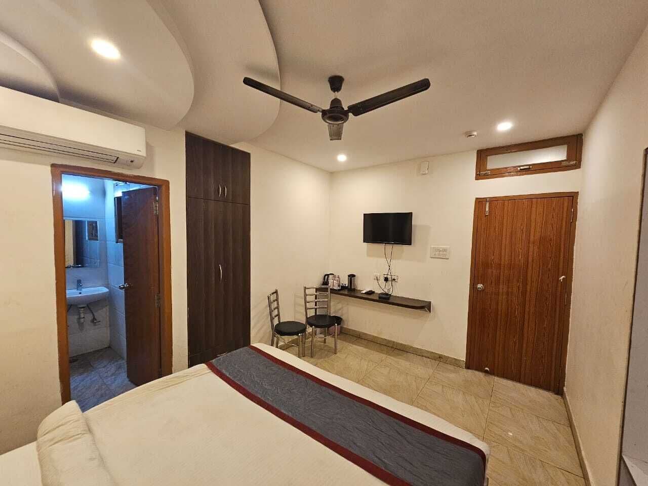 Quarto com uma cama, escrivaninha com cadeira, televisão e ventoinha no teto.