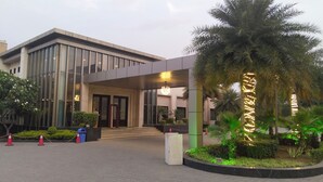 A modern building with a glass facade, a covered entrance, and a landscaped area with palm trees and shrubs. - Calista Resort (New Delhi)