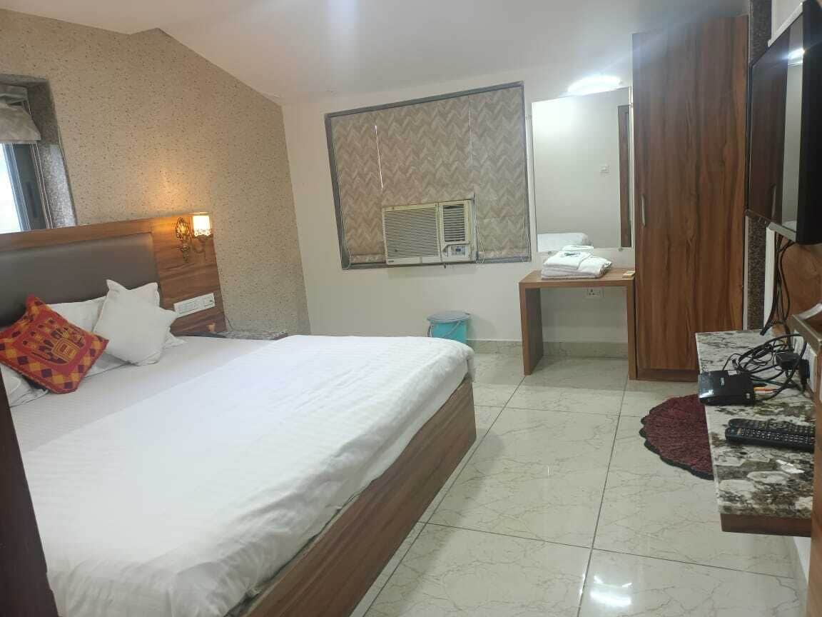 A hotel room with a bed, a desk, a chair, a mirror, and a window with blinds.