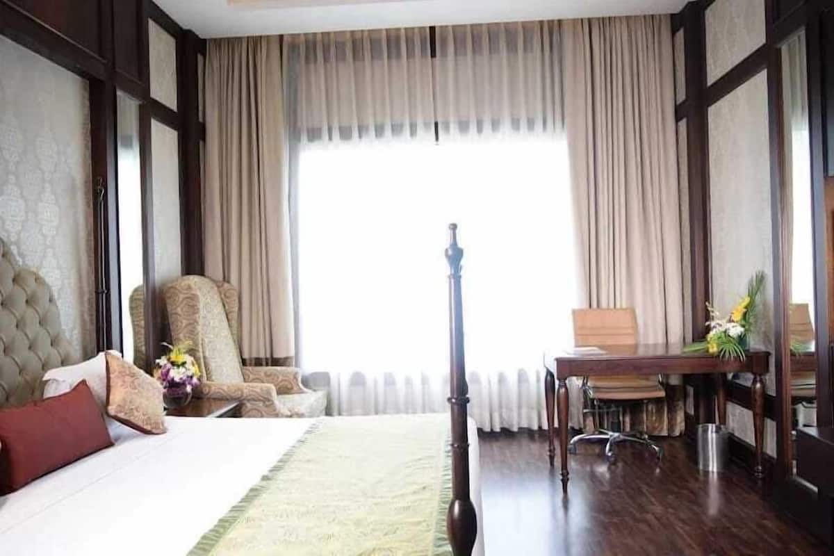 A hotel room with a bed, a chair, a desk, and a large window with curtains.
