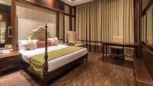 A spacious bedroom with a large bed, a sitting area, and a desk. - Calista Resort (New Delhi)