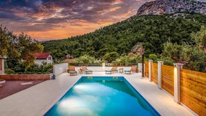 Piscina rectangular con sillas de descanso y valla de madera, rodeada de vegetación exuberante y un paisaje montañoso.