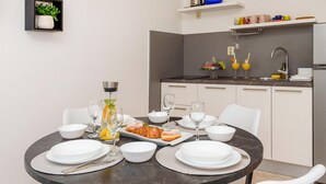 Una cocina moderna con armarios blancos, encimera negra y comedor con una mesa redonda preparada para cuatro.