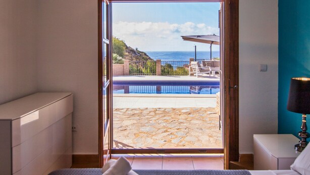 A bedroom with a large sliding glass door leading to a patio with a pool and outdoor furniture.