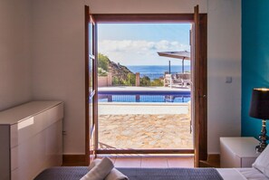 Un dormitorio con un amplio ventanal corredero que da a un patio con piscina y mobiliario exterior.