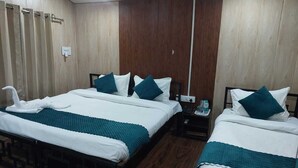 A hotel room with two beds, each with a teal blanket and pillows, a wooden wardrobe, and a nightstand with a phone and water bottles. - PRIDE INN LUXURY RESORT BY UK HEAVEN (Yamkeshwar)