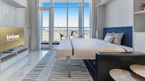 A modern hotel room with a large bed, a television, and a balcony with a view of the city.