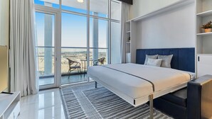 A modern hotel room with a large bed, a balcony with a view, and a small seating area.
