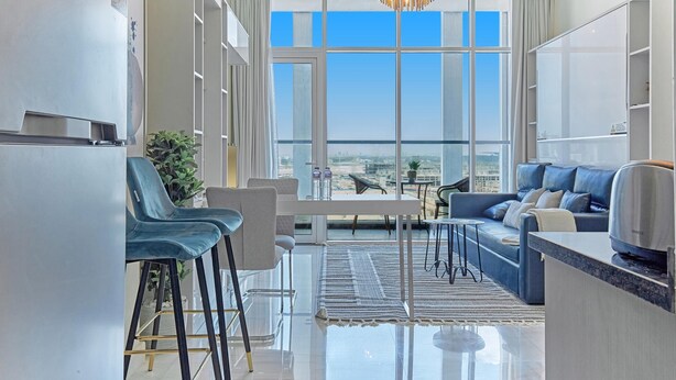 A modern living room with a large window, a dining area, and a kitchen.