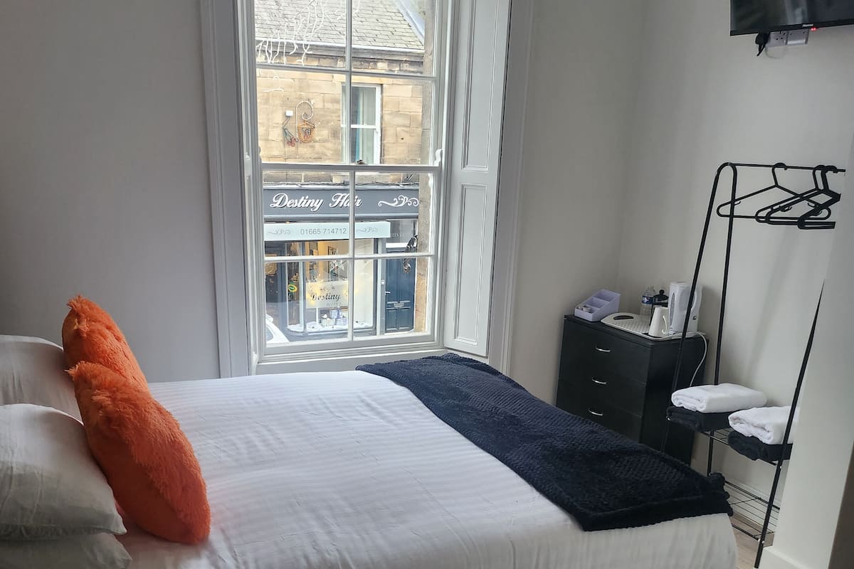 Une chambre à coucher avec un lit, une fenêtre, une commode et un téléviseur.