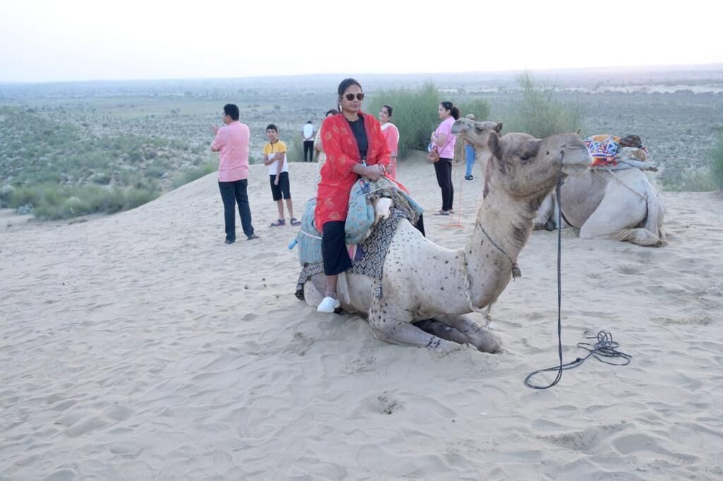 Una persona montada en un camello en un paisaje desértico, con otras personas de pie al fondo.